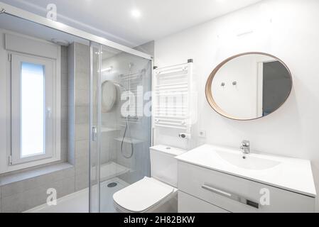 Toilette mit Dusche und wandmontiertem Heizkörper in Weißtönen mit rundem Spiegel Stockfoto