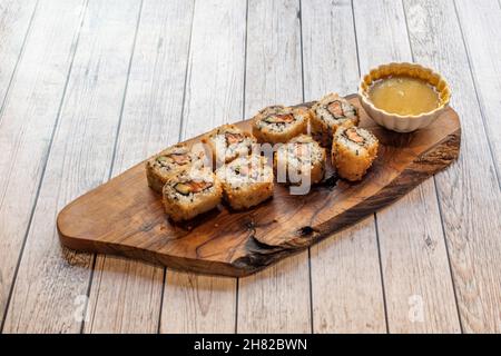 Knusprig gebratenes Uramaki-Roll-Sushi mit Lachs und Nori-Algen und curriger Sauce zum Eintauchen auf Holzteller Stockfoto