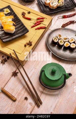 Stillleben mit grünem gusseisernen Teekannen, hölzernen Essstäbchen und Lachs Maki Sushi, Nigiri, roten Chili-Paprika, Sternanis und Bambusbrett Stockfoto