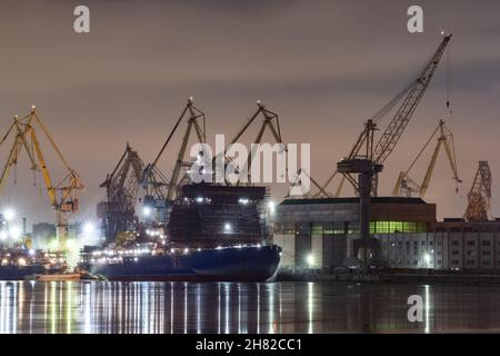 Der Bau von nuklearen Eisbrechern in der Nacht, Kräne der baltischen Werft in einem frostigen Wintertag, Dampf über dem Fluss Neva, glatte Oberfläche Stockfoto