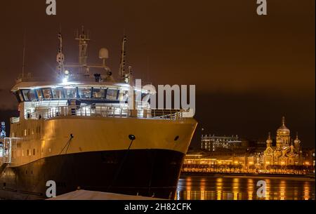 Die Panoramabilder der Winternachtstadt Sankt-Petersburg mit pittoresker Reflexion auf dem Wasser, großes Schiff, das in der Nähe der Blagoweschtschenski Brücke festgemacht wurde Stockfoto