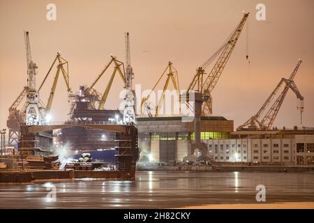 Der Bau von nuklearen Eisbrechern in der Nacht, Kräne der baltischen Werft in einem frostigen Wintertag, Dampf über dem Fluss Neva, glatte Oberfläche Stockfoto