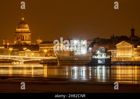 Die Panoramabilder der Winternachtstadt Sankt-Petersburg mit malerischen Spiegelungen auf dem Wasser, großes Schiff, das in der Nähe der Blagoweschtschenski Brücke oder festgemacht ist Stockfoto