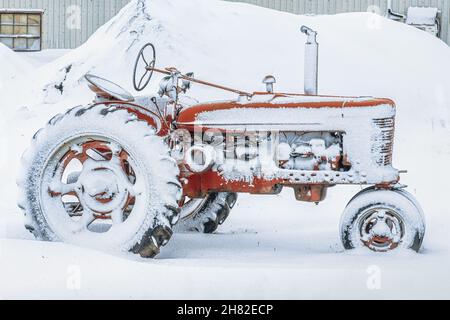 Ein alter antiker Traktor, der mit Schnee bedeckt ist. Stockfoto