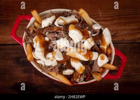 Entenconfit-Poutine-Gericht auf Holztisch Poutine ist eine kanadische Mahlzeit mit pommes Frites-Sauce und Käsekrümmen Stockfoto