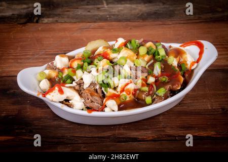 Entenconfit-Poutine-Gericht auf Holztisch Poutine ist eine kanadische Mahlzeit mit pommes Frites-Sauce und Käsekrümmen Stockfoto