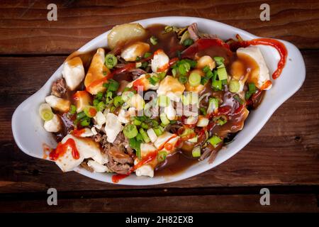 Entenconfit-Poutine-Gericht auf Holztisch Poutine ist eine kanadische Mahlzeit mit pommes Frites-Sauce und Käsekrümmen Stockfoto