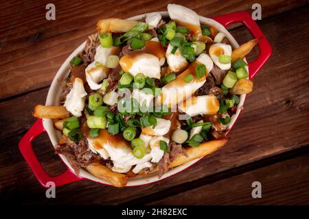 Entenconfit-Poutine-Gericht auf Holztisch Poutine ist eine kanadische Mahlzeit mit pommes Frites-Sauce und Käsekrümmen Stockfoto