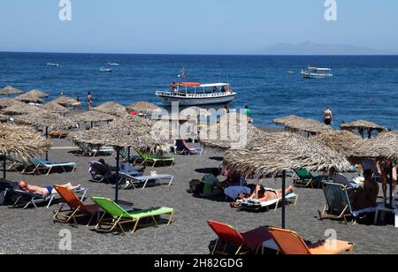 SANTORINI, GRIECHENLAND - 30. JUNI: Sonnenbaden und Schwimmen am schwarzen Strand von Kamari am 30. Juni 2012 in Santorini, Griechenland. Der Strand ist mit feinem schwarzen Sand bedeckt und fällt scharf ins Wasser ab. Stockfoto