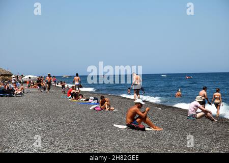 SANTORINI, GRIECHENLAND - 30. JUNI: Sonnenbaden und Schwimmen am schwarzen Strand von Kamari am 30. Juni 2012 in Santorini, Griechenland. Der Strand ist mit feinem schwarzen Sand bedeckt und fällt scharf ins Wasser ab. Stockfoto