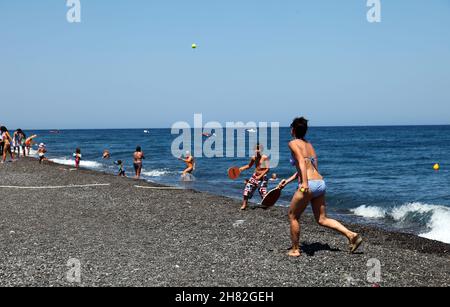 SANTORINI, GRIECHENLAND - 30. JUNI: Sonnenbaden und Tennis spielen am Kamari Beach am 30. Juni 2012 in Santorini, Griechenland. Der Strand ist mit feinem schwarzen Sand bedeckt und fällt scharf ins Wasser ab. Stockfoto