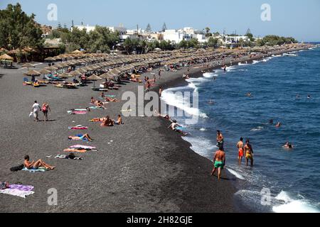 SANTORINI, GRIECHENLAND - 30. JUNI: Sonnenbaden und Schwimmen am schwarzen Strand von Kamari am 30. Juni 2012 in Santorini, Griechenland. Der Strand ist mit feinem schwarzen Sand bedeckt und fällt scharf ins Wasser ab. Stockfoto