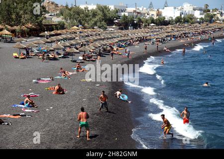 SANTORINI, GRIECHENLAND - 30. JUNI: Sonnenbaden und Schwimmen am schwarzen Strand von Kamari am 30. Juni 2012 in Santorini, Griechenland. Der Strand ist mit feinem schwarzen Sand bedeckt und fällt scharf ins Wasser ab. Stockfoto