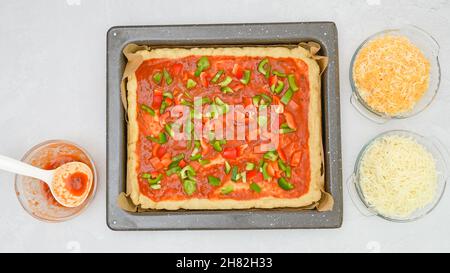 Hausgemachte vegetarische Pizza Rezept. Pizzateig mit Tomatensauce und frischem gehacktem Gemüse in der Nähe auf der Backform, flach legen Stockfoto