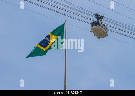 brasilianische Flagge mit Zuckerhut-Seilbahn in Rio de Janeiro, Brasilien - 23. Oktober 2021: brasilianische Flagge mit zuckerhut-Seilbahn im Hintergrund in Rio de