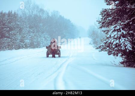 Ein Mann reitet in einem Pferdewagen auf der winterverschneiten Straße Stockfoto