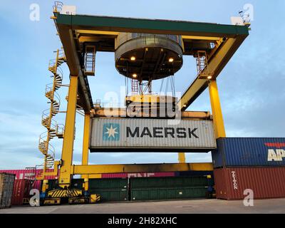 Ein Maersk-Transportcontainer, der von einem Kran an einem Warenterminal oder Dock auf einen Güterzug geladen wird Stockfoto