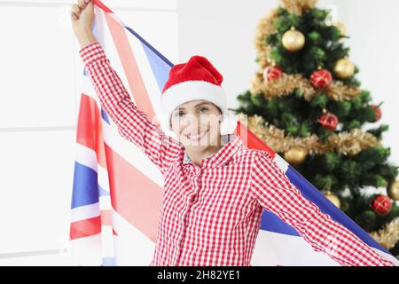 Lächelnde Frau hält Feuchtigkeit UK vor dem Hintergrund des Neujahrsbaums Stockfoto