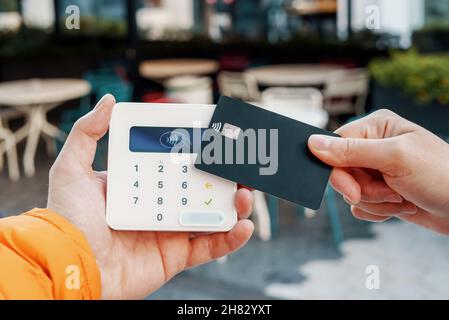 Unbekennbare weibliche Kundin mit einer Kreditkarte ausschneiden, die kontaktlos am POS-Terminal im Straßencafé bezahlt Stockfoto