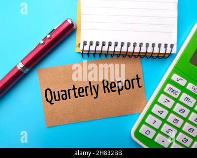 Stift, Notizbuch, Taschenrechner und braune Karte mit Text Quarterly Report geschrieben. Stockfoto