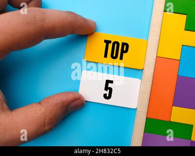 Hand hält farbigen Holzwürfel mit Wort TOP 5 auf blauem Hintergrund. Stockfoto