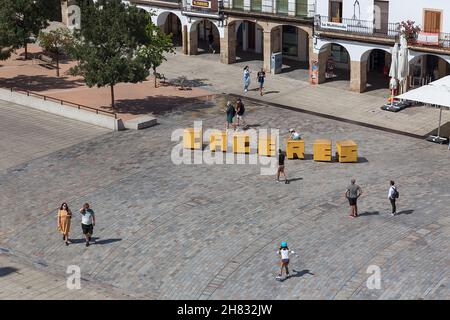 Cáceres Spanien - 09 12 2021: Luftaufnahme mit Touristen, die auf einem zentralen Platz spazieren, Plaza Mayor in Cáceres, gelbe dekorative Buchstaben mit dem Stockfoto