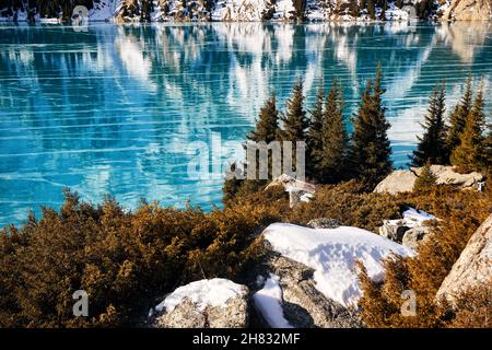 Schöne Landschaft von Bergsee mit blauem Eis und Fichtenwald im Winter Stockfoto