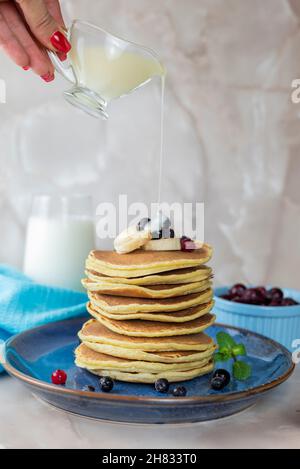 Ein Mädchen gießt kondensierte Milchpfannkuchen auf Backwaren mit Beeren und einer Banane Stockfoto