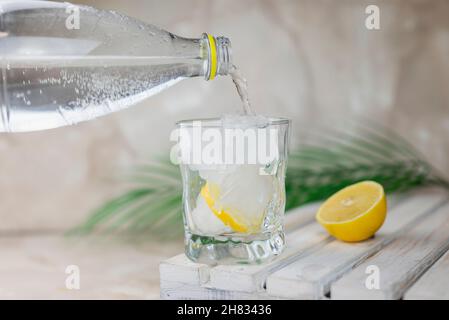 Wasser oder Tonic wird aus einer Flasche in ein Glas mit Eis und Zitrone gegossen Stockfoto