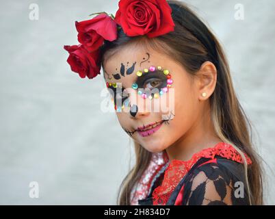 Hübsch verkleidetes mexikanisches Yucatecan Pre-Teen-Mädchen mit traditionellem Catrina Face Make-up und Glitzergesicht-Juwelen am Tag der Toten schaut den Betrachter an. Stockfoto