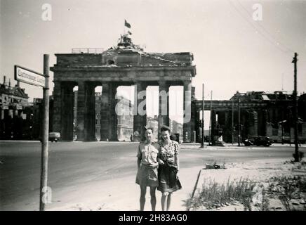 Im August 1947 besuchte der RAF-Pilot Browne Berlin und nahm eine Begleiterin mit auf eine Sightseeing-Tour durch die Stadt. Hier stellen sie sich vor dem von der Schlacht gezeichneten Brandenburger Tor. Das Mädchen ist unbekannt, möglicherweise eine Kellnerin, die an ihrer Schürze vorbei geht. P/O Browne flog am 12th. August 1947 nach Berlin Gatow und am 19th. August 1947 nach RAF Bückeberg. Stockfoto