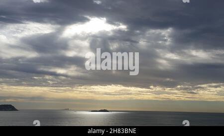 Schöner Sonnenaufgang mit den ersten Sonnenstrahlen, die eine kleine Insel im Ozean erleuchten, Guarujá, São Paulo, Brasilien. Stockfoto