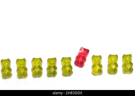 Eine Reihe grüner Gummibären, in denen sich ein roter Kerl aus einem Konzept für Individualität und Anderssein anders verhält, wird auf einem weißen Rückengr isoliert Stockfoto