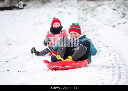 Cradley Heath, West Midlands, Großbritannien. 27th. November 2021. Zwei junge Mädchen fahren auf den verschneiten Hängen im Haden Hill Park, Cradley Heath, in den West Midlands zu ihren Schlitten. Kredit: Peter Lopeman/Alamy Live Nachrichten Stockfoto