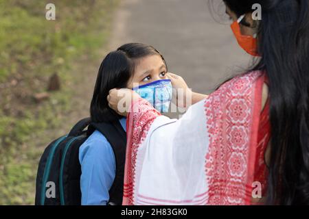 Ein indisches Schulkind, das nach einer Pandemie wieder zur Schule geht, wobei ihre Mutter Nasenmaskenschutz trägt Stockfoto