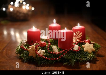 Vierter Advent - geschmückter Adventskranz aus Tannenzweigen mit roten brennenden Kerzen auf einem Holztisch in der Zeit vor Weihnachten, festliches Bokeh in Th Stockfoto