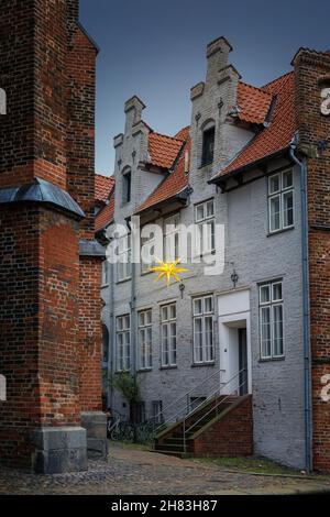 Leuchtender mährischer Stern als Advent- und weihnachtsdekoration in einer engen Gasse mit historischen Backsteinhäusern in der Altstadt von Lübeck, ausgewählt Stockfoto