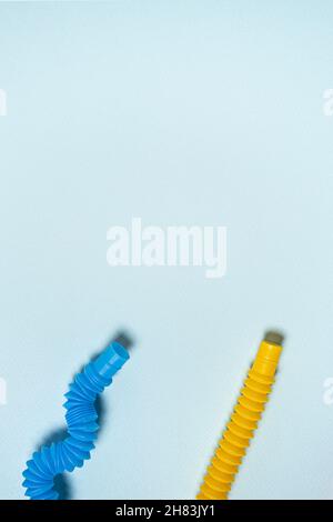 Gerade und gebogen in Wellenform bunt leuchtend gelb und blau Pop-Rohr Kinder Spielzeug. Zwei kontrastierende Kunststoff-Antistress-Spielzeuge auf blauem Papierhintergrund Stockfoto
