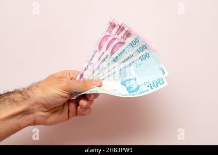 Mann, der türkische Lira vor einer weißen Wand hält Stockfoto