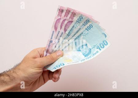 Mann, der türkische Lira vor einer weißen Wand hält Stockfoto