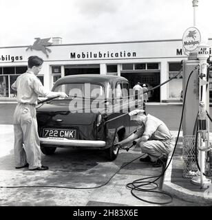 1950s, zwei uniformierte Vorhofmitarbeiter an einer neuen Mobilgas-Tankstelle, neben einem Auto in Austin, das von einem mit Benzin befüllt und der andere seinen Reifendruck überprüft, England, Großbritannien. Ein amerikanisches Ölunternehmen, Vacuum Oil, hat 189 die Marke „Mobilgas“ eingetragen. Sie fusionierte 1931 mit Socony und wurde 1955 zur Socony Mobil Oil Company. Die ersten britischen Tankstellen wurden Anfang 1950s eröffnet und waren voll mit Pumpenwartern und Mechanikern besetzt. In den Nachkriegsjahren stieg der Kfz-Absatz deutlich an, und Großbritannien wurde nach den USA zum zweitgrößten Automobilhersteller der Welt. Stockfoto