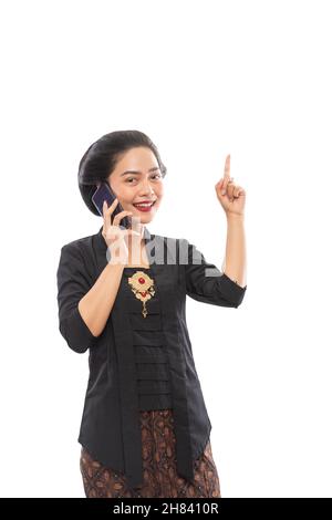 Frau in Kebaya präsentiert Kopierraum beim Telefonieren Stockfoto