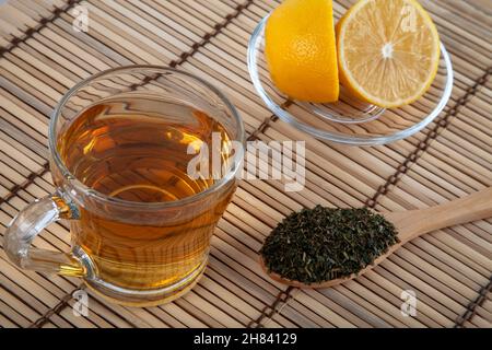 Tasse grüner Tee, Zitronenscheiben, trockene Blätter auf einem Weidenkorb Stockfoto