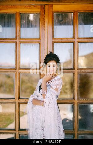 Junge Frau in Spitzenkleid steht neben Glastür Stockfoto