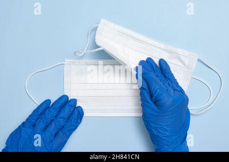 Hand in medizinischen Handschuhen hält zwei weiße medizinische Gesichtsmasken auf blauem Hintergrund Stockfoto