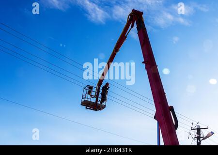 Elektriker arbeiten in der Höhe auf hydraulischer Antennenbühne gegen blauen Himmel Stockfoto