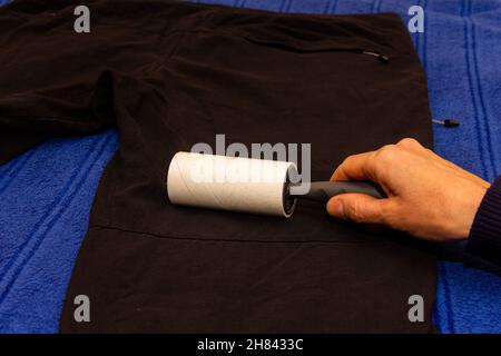 Weibliche Hand mit Haftwalze zum Reinigen von Kleidung reinigt die schwarze Herrenhose aus nächster Nähe Stockfoto