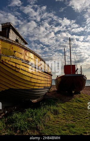 Zwei Fischerboote, eines ist gelb und das andere flach, ruhen auf Gras am Strand in der Hastings Old Town unter blauem Himmel in Hastings, Großbritannien Stockfoto