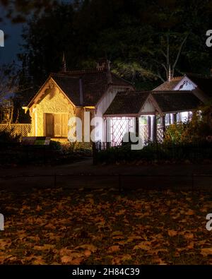 Eine Nachtaufnahme des Duck Island Cottage, St James's Park, beleuchtet durch warmes gelbes Licht mit rot/orangen Platanenblättern auf dem Boden. Stockfoto