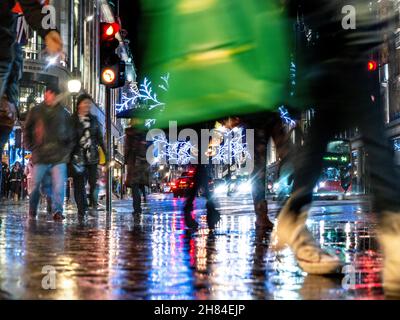 Weihnachtseinkäufer Regenregen Reflexionen geschäftige Szene von regnerischen Straßenverkehr und Regenschirme in einem regen fegte Regent Street mit Weihnachtsbeleuchtung hinter London UK Stockfoto